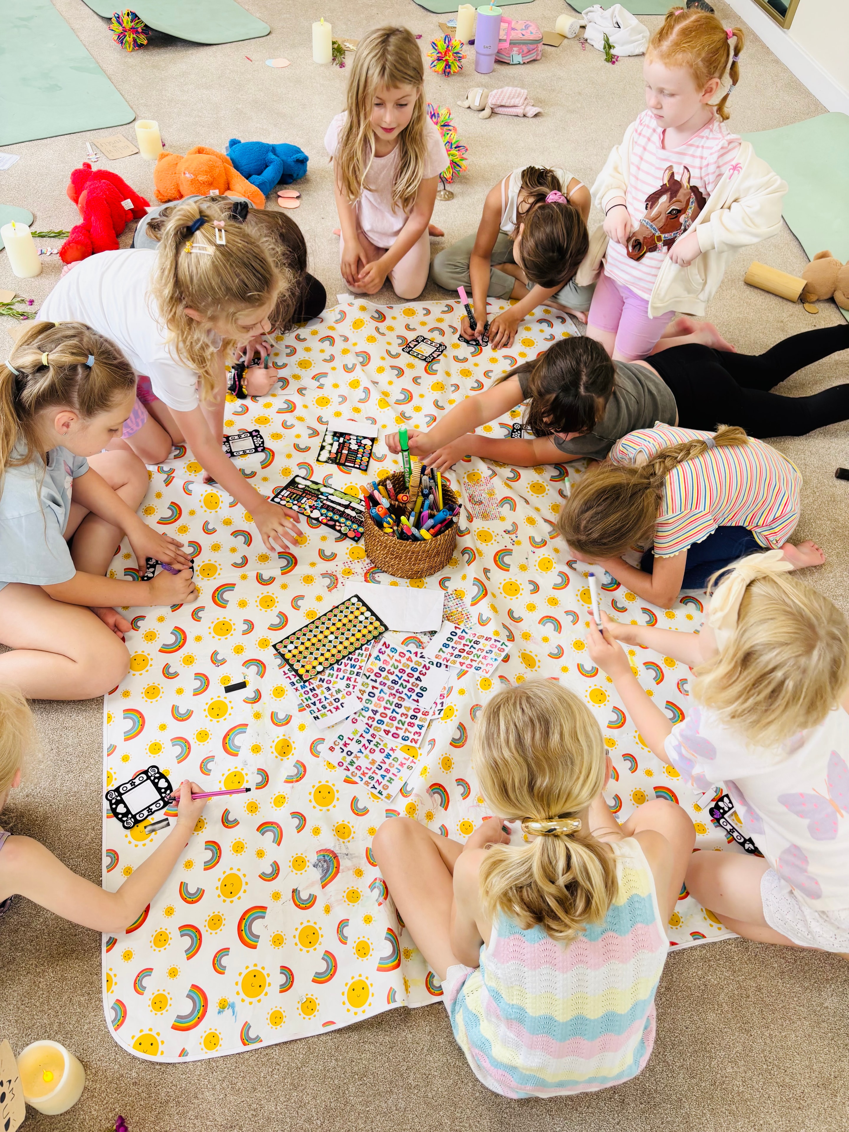 Children gathered around a rainbow blanket doing crafts at Buddha Bears